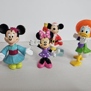 Op de afbeelding: Een set van zes Disney-figuren, waaronder Mickey Mouse, Minnie Mouse, Donald Duck, Goofy, Pluto en Daisy Duck. De figuren zijn gemaakt van plastic en zijn felgekleurd. Ze staan ​​allemaal in verschillende poses.