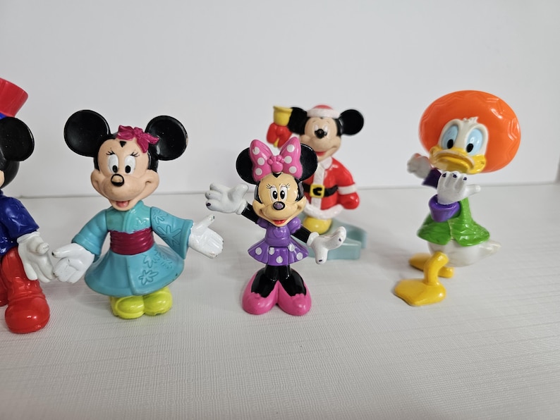 Op de afbeelding: Een set van zes Disney-figuren, waaronder Mickey Mouse, Minnie Mouse, Donald Duck, Goofy, Pluto en Daisy Duck. De figuren zijn gemaakt van plastic en zijn felgekleurd. Ze staan ​​allemaal in verschillende poses.