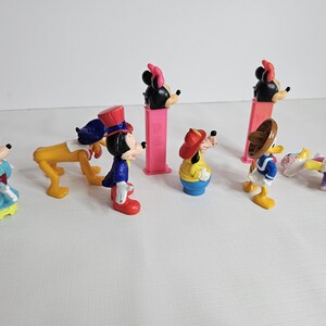 K&ouml;nnte beinhalten: Ein Set mit acht Vintage-Disney-Figuren, darunter Mickey Mouse, Minnie Mouse, Goofy und Donald Duck. Die Figuren sind aus Kunststoff und in gutem Zustand. Sie tragen alle ihre charakteristischen Outfits und haben leuchtende Farben.