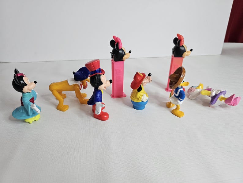 K&ouml;nnte beinhalten: Ein Set mit acht Vintage-Disney-Figuren, darunter Mickey Mouse, Minnie Mouse, Goofy und Donald Duck. Die Figuren sind aus Kunststoff und in gutem Zustand. Sie tragen alle ihre charakteristischen Outfits und haben leuchtende Farben.