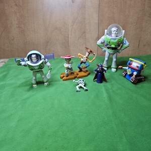 May include: A collection of seven toy figures from the Toy Story franchise. The figures include Buzz Lightyear, Woody, Jessie, Rex, Zurg, and a robot. The figures are all in different poses and are made of plastic.