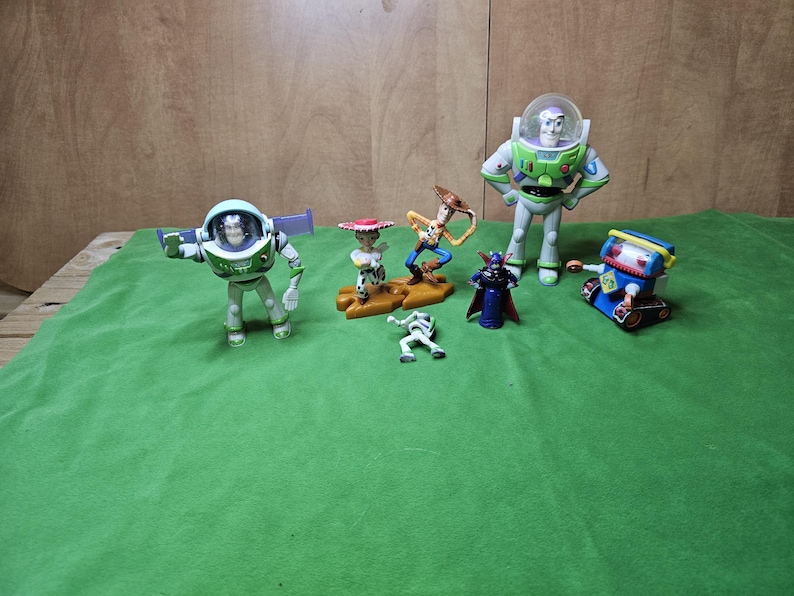 May include: A collection of seven toy figures from the Toy Story franchise. The figures include Buzz Lightyear, Woody, Jessie, Rex, Zurg, and a robot. The figures are all in different poses and are made of plastic.