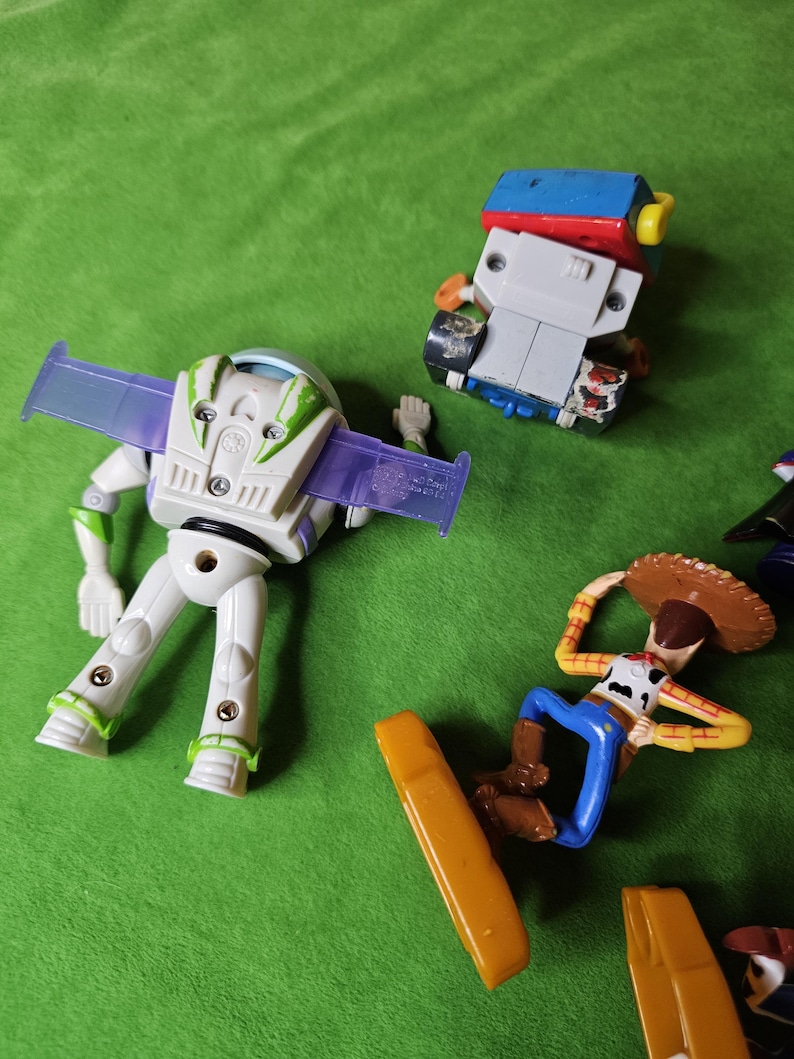May include: A set of four plastic toy figures from the Toy Story franchise. The figures include Buzz Lightyear, Woody, and two other characters. The figures are all in different poses and are made of a variety of colours, including green, blue, red, yellow, and brown.