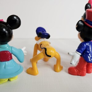 K&ouml;nnte beinhalten: Ein Set mit f&uuml;nf kleinen Plastikfiguren von Disney-Charakteren. Die Figuren umfassen Mickey Mouse in einem blau-wei&szlig;en Outfit, Minnie Mouse in einem blau-roten Kimono, Pluto mit einem blauen Hut, Goofy in einem rot-blauen Outfit und Donald Duck in einem rot-wei&szlig;en Outfit.