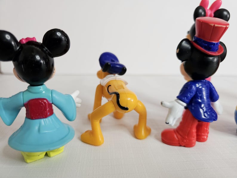 K&ouml;nnte beinhalten: Ein Set mit f&uuml;nf kleinen Plastikfiguren von Disney-Charakteren. Die Figuren umfassen Mickey Mouse in einem blau-wei&szlig;en Outfit, Minnie Mouse in einem blau-roten Kimono, Pluto mit einem blauen Hut, Goofy in einem rot-blauen Outfit und Donald Duck in einem rot-wei&szlig;en Outfit.