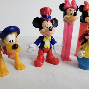 K&ouml;nnte beinhalten: Eine Sammlung von Vintage-Disney-Figuren, darunter Mickey Mouse, Minnie Mouse, Pluto und Goofy. Die Figuren sind aus Kunststoff und in verschiedenen Farben, darunter Rot, Blau, Gelb und Schwarz.