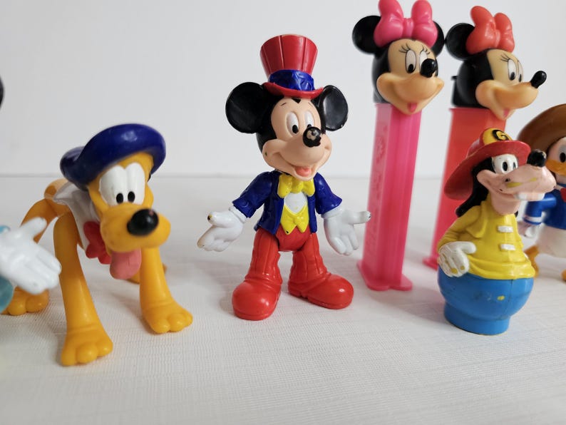 K&ouml;nnte beinhalten: Eine Sammlung von Vintage-Disney-Figuren, darunter Mickey Mouse, Minnie Mouse, Pluto und Goofy. Die Figuren sind aus Kunststoff und in verschiedenen Farben, darunter Rot, Blau, Gelb und Schwarz.