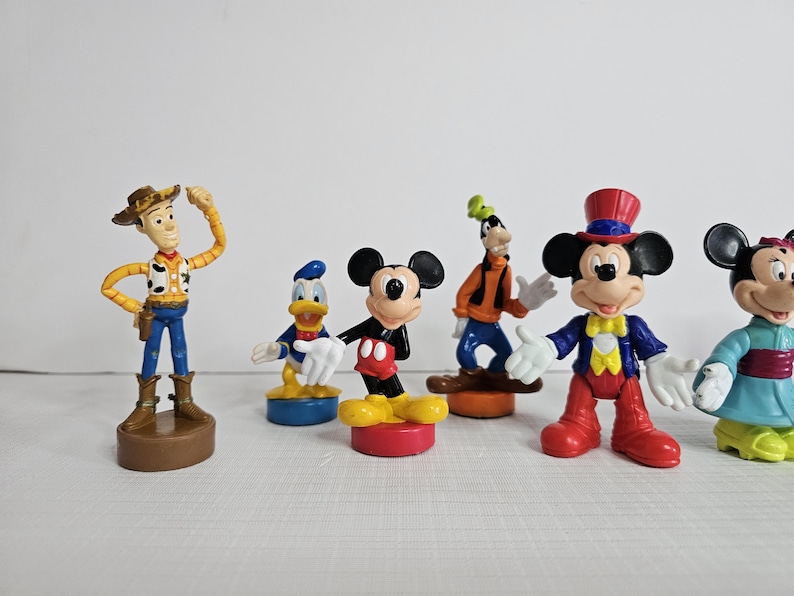 Op de afbeelding: Een set van zeven plastic Disney-figuren, waaronder Mickey Mouse, Minnie Mouse, Donald Duck, Goofy en Woody. De figuren zijn kleurrijk en gedetailleerd en zouden een geweldige aanvulling zijn op elke Disney-collectie.