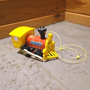 May include: A yellow and red toy train with the text "TOOT-TOOT" on the side. The train has black wheels and a black smokestack. A yellow string is attached to the front of the train.