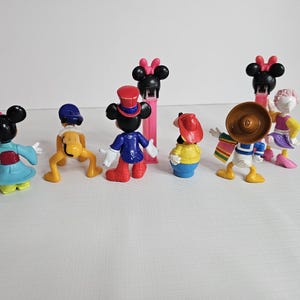 K&ouml;nnte beinhalten: Ein Set mit acht kleinen Disney-Figuren aus Plastik. Die Figuren umfassen Mickey Mouse, Minnie Mouse, Donald Duck, Goofy, Pluto und Daisy Duck. Die Figuren sind alle in verschiedenen Posen und sind bunt.