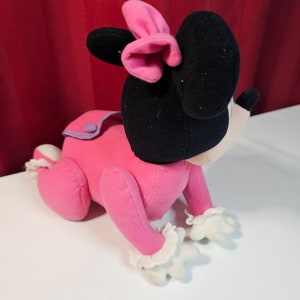 K&ouml;nnte beinhalten: Rosa Pl&uuml;schtier einer Comicmaus mit schwarzen Ohren und einer rosa Schleife. Die Maus krabbelt auf allen vieren.