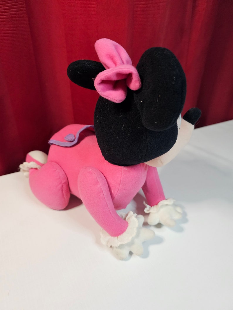 K&ouml;nnte beinhalten: Rosa Pl&uuml;schtier einer Comicmaus mit schwarzen Ohren und einer rosa Schleife. Die Maus krabbelt auf allen vieren.