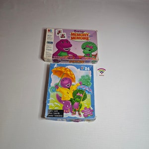 Può includere: Due giochi di memoria vintage a tema Barney il Dinosauro. Una scatola presenta Barney e Baby Bop, con la scritta "Barney Memory Memoire". L'altra scatola è un puzzle con Barney e Baby Bop sotto la pioggia, con il numero 24.