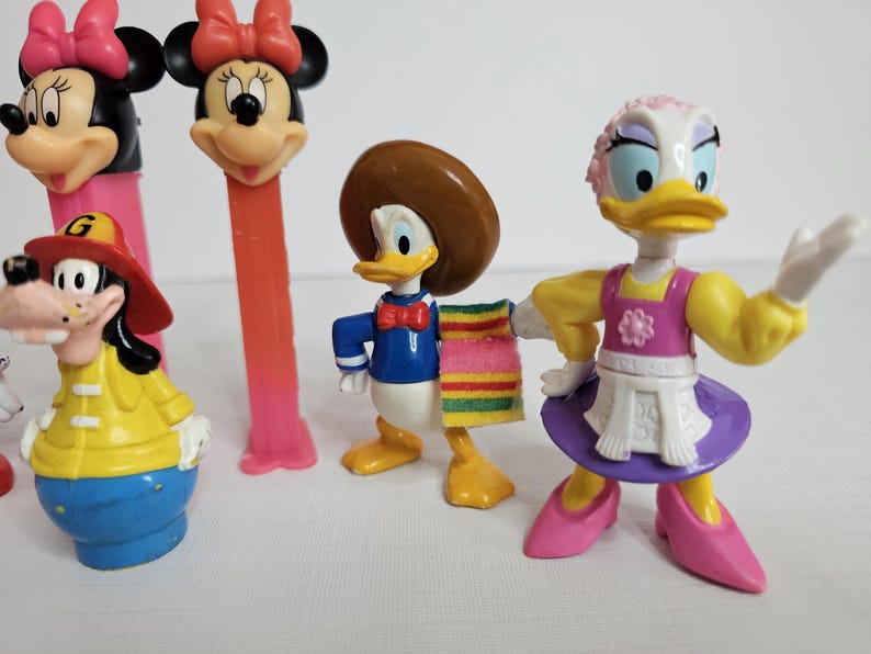 K&ouml;nnte beinhalten: Eine Sammlung von Disney-Figuren, darunter Mickey Mouse, Minnie Mouse, Donald Duck und Daisy Duck. Die Figuren sind aus Kunststoff und bunt.