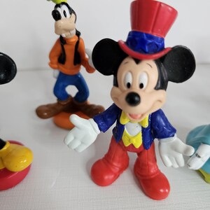 Op de afbeelding: Een set van vijf plastic Disney-figuren. De figuren zijn Mickey Mouse met een rood-wit-blauwe hoed, Goofy met een groene hoed, Minnie Mouse met een blauwe jurk, Donald Duck met een matrozenpak en Pluto met een rode halsband.