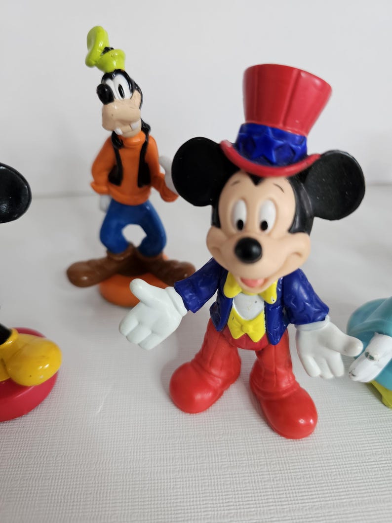 Op de afbeelding: Een set van vijf plastic Disney-figuren. De figuren zijn Mickey Mouse met een rood-wit-blauwe hoed, Goofy met een groene hoed, Minnie Mouse met een blauwe jurk, Donald Duck met een matrozenpak en Pluto met een rode halsband.