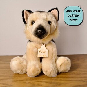 May include: A plush German Shepherd dog with a cream and black coat, sitting upright. It has a wooden tag around its neck that says "Your name". A blue speech bubble with the text "ADD YOUR CUSTOM TEXT!" is in the background.
