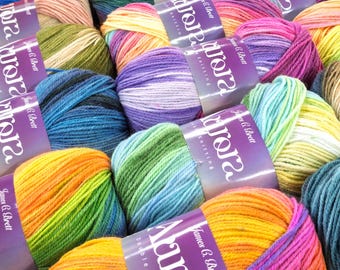 May include: A collection of colorful yarn skeins, featuring a variety of hues including blues, greens, oranges, and purples. Each skein is wrapped with a label that reads "James C. Brett Aurora Knitting". The yarn appears soft and suitable for knitting projects.