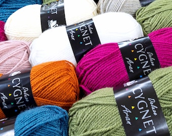 May include: A collection of colorful yarn skeins in various shades, including white, pink, orange, green, and blue. Each skein is labeled with "Deluxe CYGNET Aran". The yarn is tightly wound, suggesting it's suitable for knitting or crochet projects.