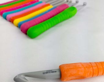 May include: A collection of colorful crochet hooks with ergonomic handles. The hooks are in various bright colors, including green, pink, yellow, and orange. One hook is in focus, showing the size: U.S. M/N-13/9.00 mm.