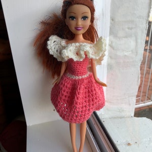 May include: A doll with long red hair wearing a pink crocheted dress with a white crocheted collar.