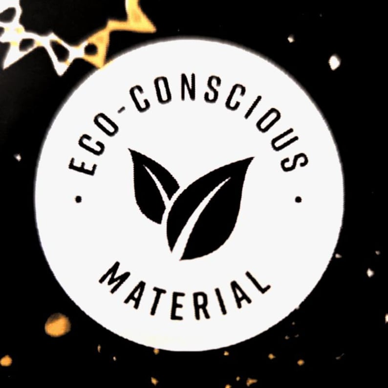 A white circular emblem with the words "ECO-CONSCIOUS MATERIAL" in black, surrounding a pair of black leaves. The background is black with gold flecks.