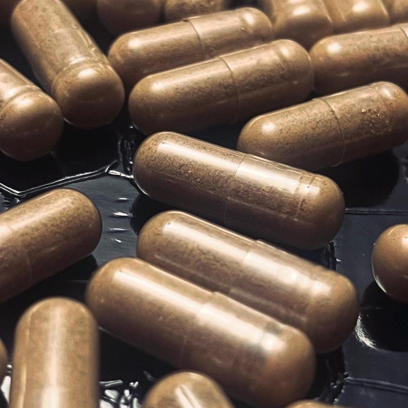 This image is a close up photo of Voacanga Africana root bark in vegetarian capsules on a shiny black geometric background.