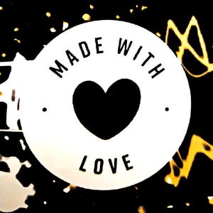 May include: A circular white label featuring a black heart icon in the center. The text MADE WITH LOVE is printed in black capital letters around the heart. The background is black with abstract yellow and white paint splatter patterns.