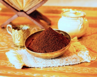 Könnte beinhalten: Nahaufnahme einer kleinen, runden, goldfarbenen Schale, gefüllt mit dunkelbraunen Kaffeepulvern. Die Schale steht auf einem weißen, gefranstem Tuch auf einer Holzoberfläche.