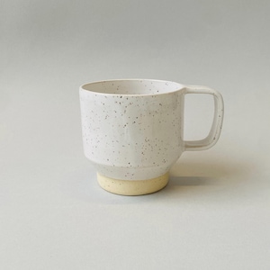 May include: White ceramic mug with a speckled design and a light yellow base. The mug has a square handle and a cylindrical shape. The mug is designed for hot or cold beverages.