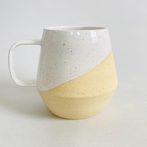 May include: A set of three ceramic mugs with a speckled, matte finish. The mugs are in shades of cream, light gray, and dark gray. Each mug has a simple, minimalist design and a rounded handle. Perfect for coffee or tea.