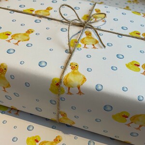 May include: White wrapping paper with a repeating pattern of yellow rubber duckies and blue bubbles. The paper is tied with twine.