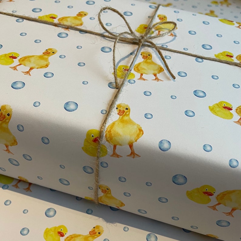 May include: White wrapping paper with a repeating pattern of yellow rubber duckies and blue bubbles. The paper is tied with twine.