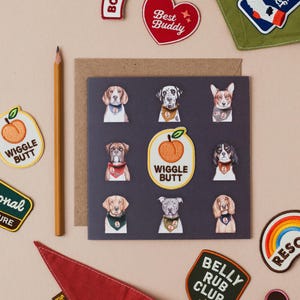 Könnte beinhalten: Eine Sammlung von Aufnähern zum Thema Hunde und eine Grußkarte. Die Aufnäher enthalten Sätze wie "Boopable", "Best Buddy" und "Belly Rub Club". Die Karte zeigt Illustrationen verschiedener Hunderassen. Ein Bleistift und ein rotes Bandana sind ebenfalls vorhanden.