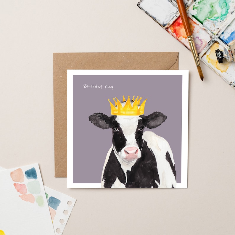 May include: A birthday card featuring a black and white cow wearing a gold crown. The card has a purple background and the text "Birthday King" at the top.