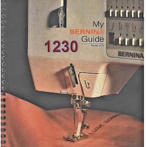 以下が含まれることがあります： 白いベルニナ1230ミシンをクローズアップした写真。側面には「My Bernina Guide Model 1230」の文字が印刷されています。ミシンはピンクの布に「I Love Bernina」の文字を縫っています。