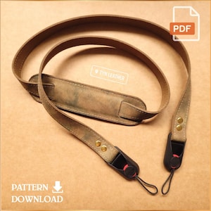 Puede incluir: Una correa de cámara de cuero marrón con un acabado envejecido. La correa presenta una almohadilla ancha para el hombro y extremos ajustables con remaches metálicos y conectores negros. El texto "TYN LEATHER" es visible. Las palabras "PATTERN DOWNLOAD" también son visibles.