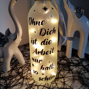 Könnte beinhalten: Eine dekorative Glasflasche mit einer Lichterkette im Inneren, mit dem deutschen Text "Ohne Dich ist die Arbeit nur halb so schön" in Schwarz. Die Flasche ist mit Sternaufklebern und einem dekorativen Kragen verziert.