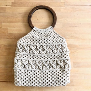 Peut inclure: Un sac cabas en macramé beige avec une anse en bois.