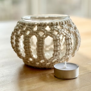 以下が含まれることがあります： ガラス製のインサートと白いティーライトキャンドルが付いた、白いクロシェのキャンドルホルダーです。