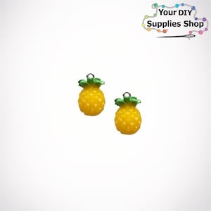 May include: Two yellow pineapple charms with green leaves. The charms have a hole at the top for attaching to a necklace, bracelet, or other jewelry.