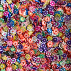 Op de afbeelding: Een grote verzameling kleurrijke polymer clay bloembedels in verschillende tinten roze, paars, oranje, geel, groen, blauw en wit. De bloemen zijn allemaal in verschillende maten en vormen en perfect om een vleugje whimsy toe te voegen aan elk knutselproject.