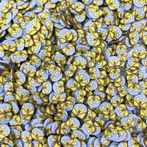 May include: A large quantity of small, round, ceramic embellishments. Each embellishment is a light blue and yellow alien face with black eyes and a black outline.