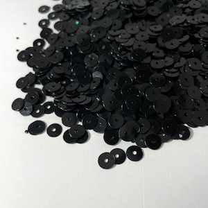 以下が含まれることがあります： 白い表面に散らばった、黒い丸いスパンコールの大きな山