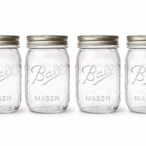 May include: Four clear glass Ball Mason jars with silver-colored lids. The jars have the Ball logo and the word "MASON" embossed on the front. The jars are empty and sit on a white background.
