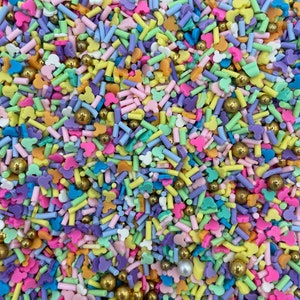 May include: A colorful mix of sprinkles featuring pastel-colored Mickey Mouse heads, stars, and long, thin sprinkles. The sprinkles are a mix of light pink, light blue, light green, yellow, and purple.