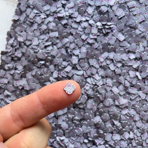 May include: A close-up of a pile of silver glitter with a pink Hello Kitty design. The glitter is small and scattered on a white surface.