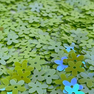 May include: A pile of green iridescent flower-shaped sequins. The sequins have a light green color with a slight iridescent sheen.