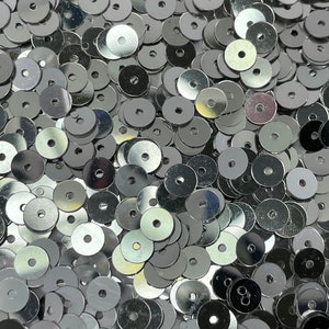 May include: A large pile of silver round sequins. The sequins are shiny and have a hole in the center.