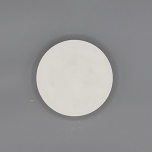 May include: A plain, white, circular object, possibly a coaster or a small plate, is centered against a gray background. The object's surface appears smooth and matte. The lighting is even, casting no shadows.